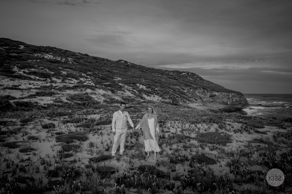 A couple holding hands among coastal plants in black and white