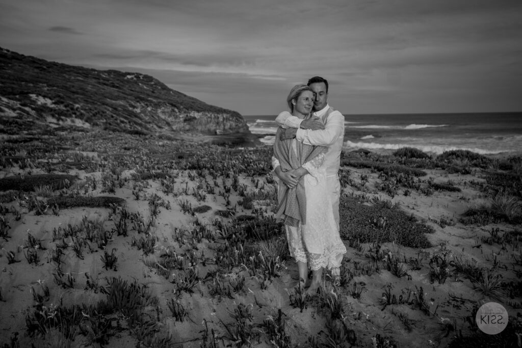 A wedding couple embracing beside the coast in black and white