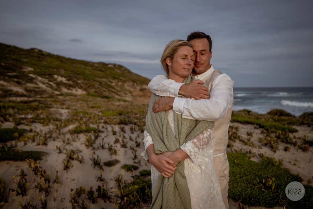A close portrait of a couple embracing beside the coast