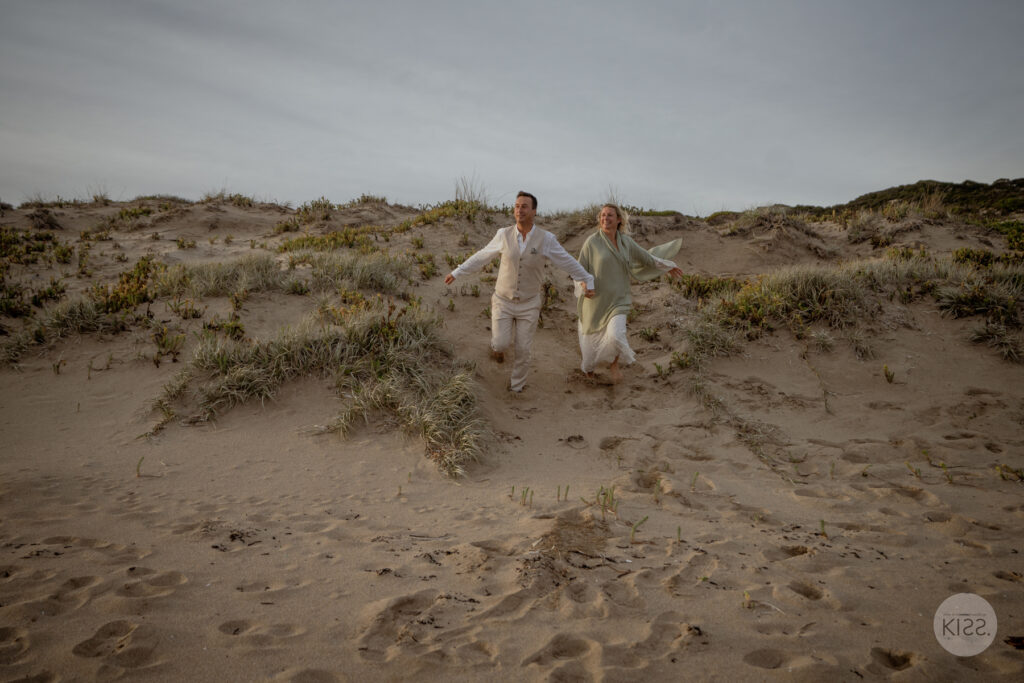 A couple running hand in hand through coastal dunes