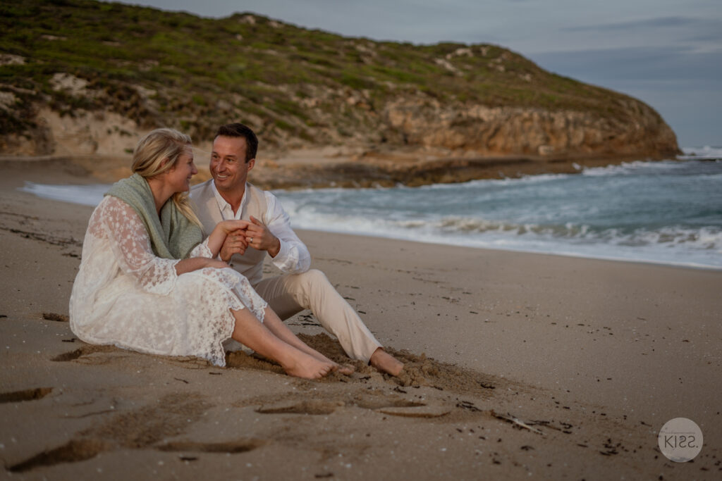 A wedding couple sitting close together on the sand