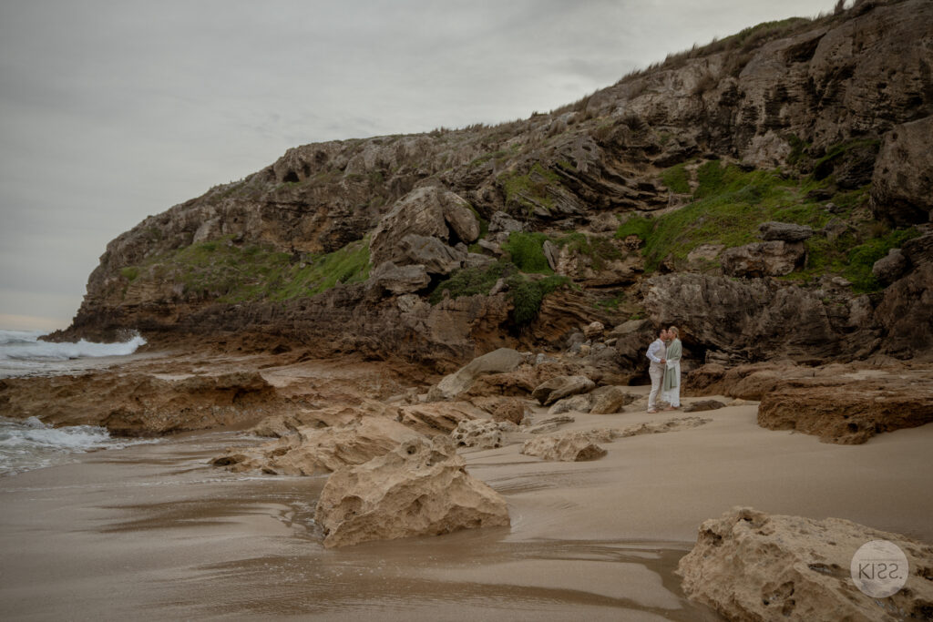 A wedding couple at a sandy cove beneath a headland