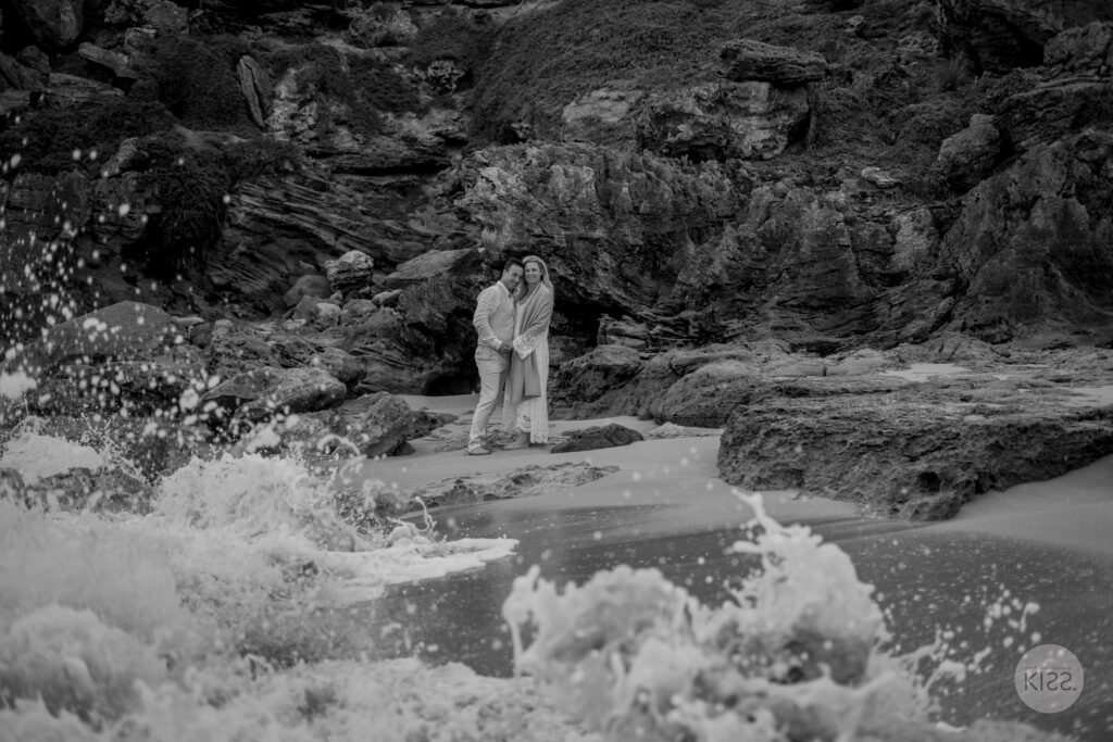 A wedding couple beside breaking waves in black and white