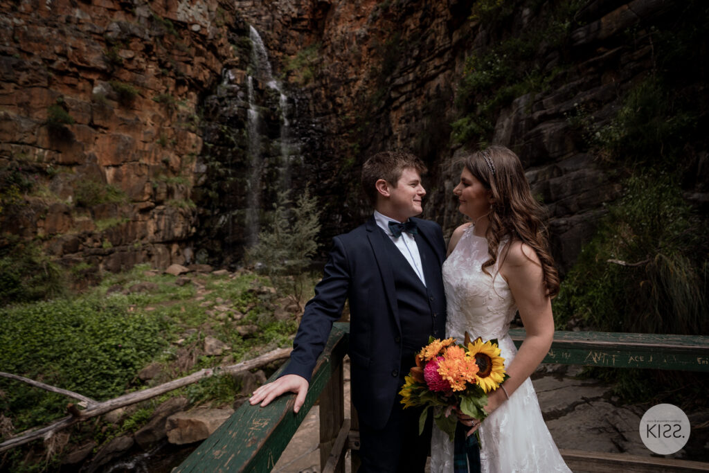 A wedding couple standing together beside a bridge railing