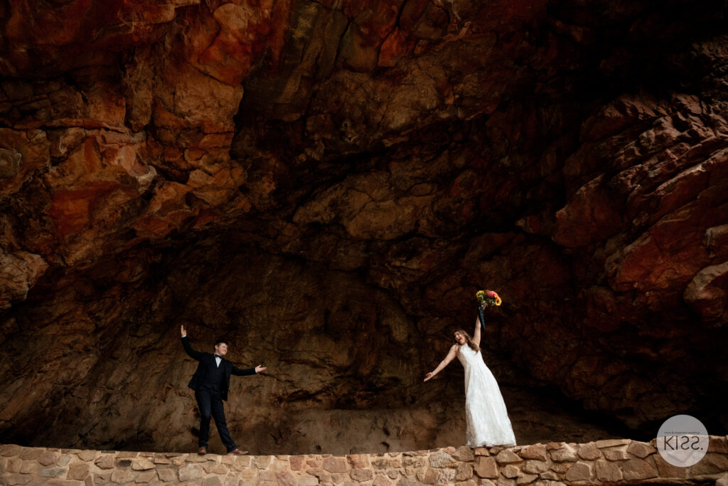 A wedding couple standing beneath a broad orange rock overhang