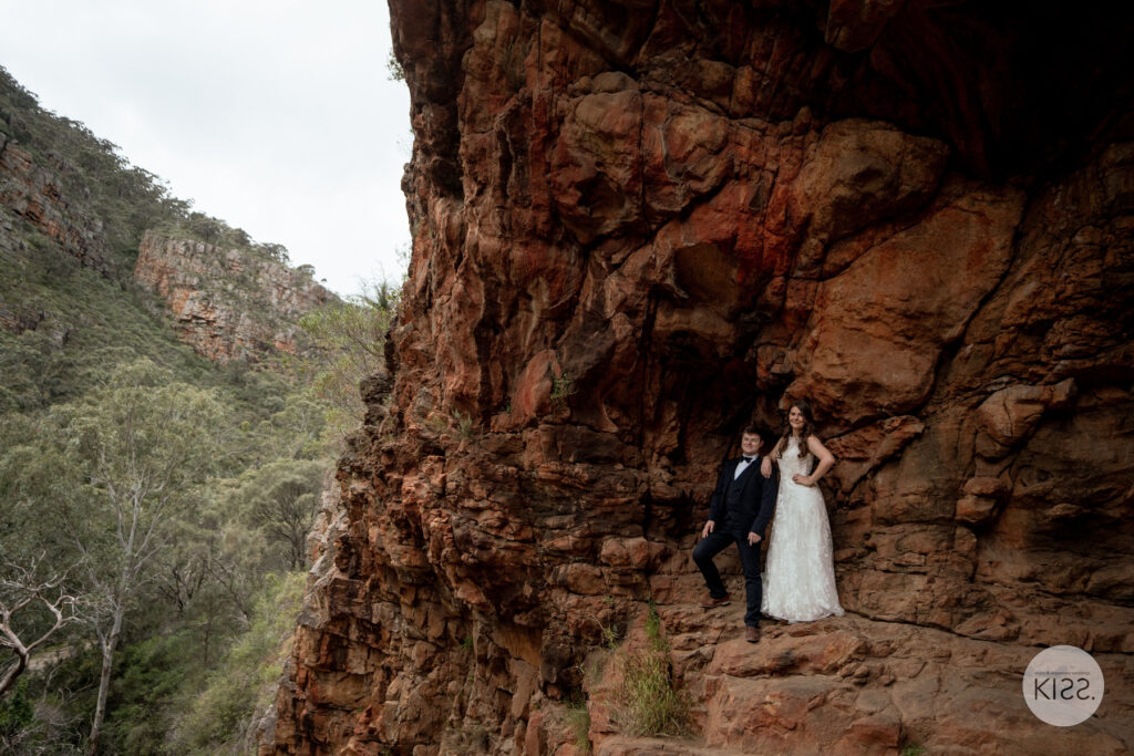A wedding couple embracing at the entrance to a rocky cave