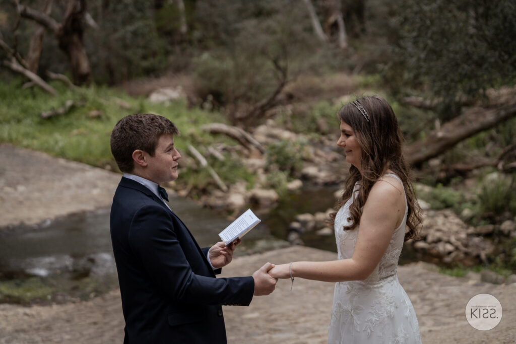 A groom reading his vows beside a woodland creek