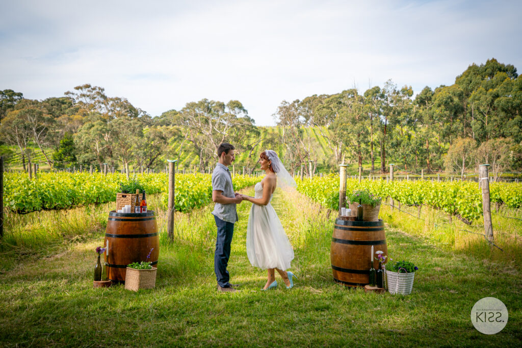 A KISS wedding couple among vineyard rows beside wine barrels