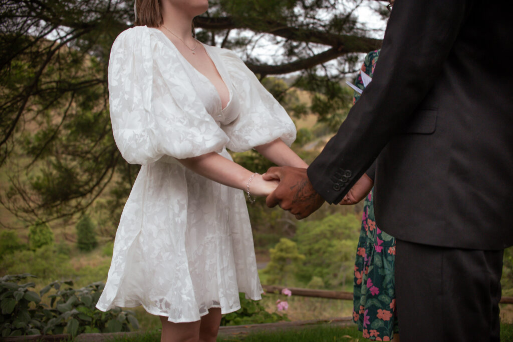 A bride in a short white dress holding hands with her partner
