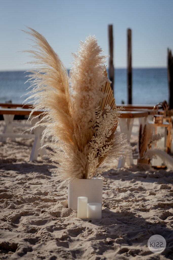 Dried flower arrangement and lantern beside a beach wedding aisle