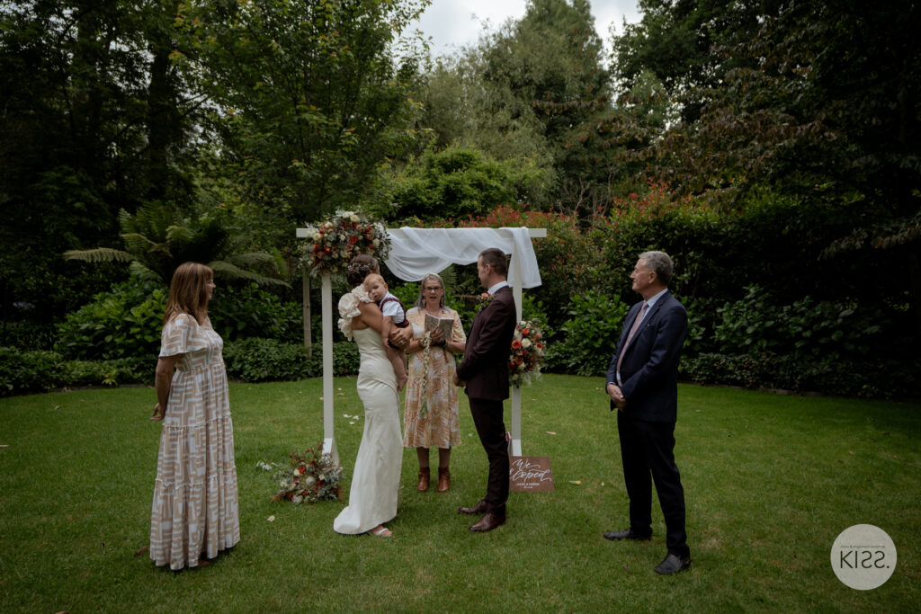 A small wedding party gathered beneath a garden arbour