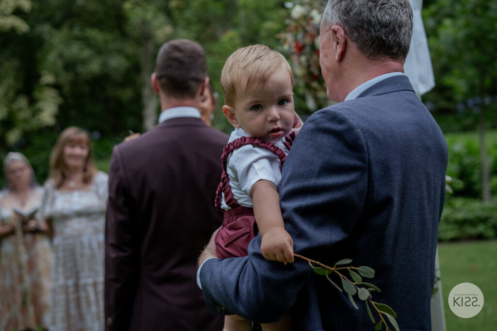 A guest holding a baby during a garden wedding ceremony