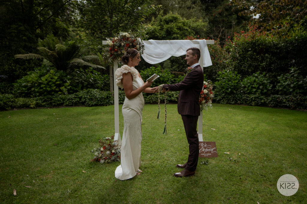 A couple exchanging rings beneath a floral arbour