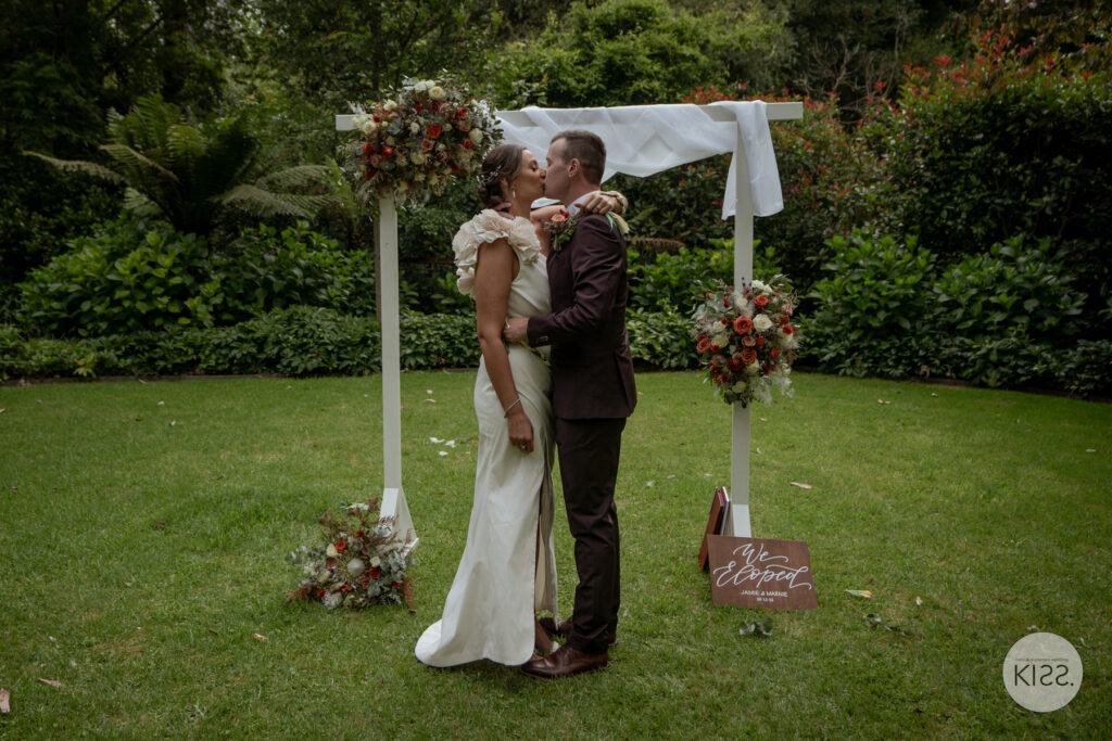 A couple kissing beneath their garden wedding arbour