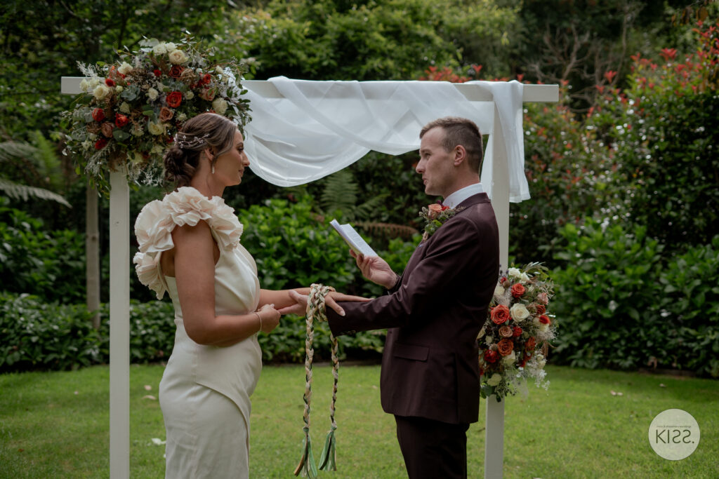 A couple holding hands beneath a white wedding arbour