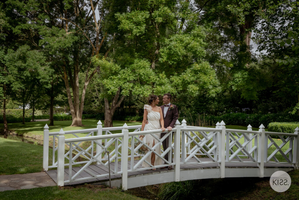A wedding couple crossing a white garden footbridge