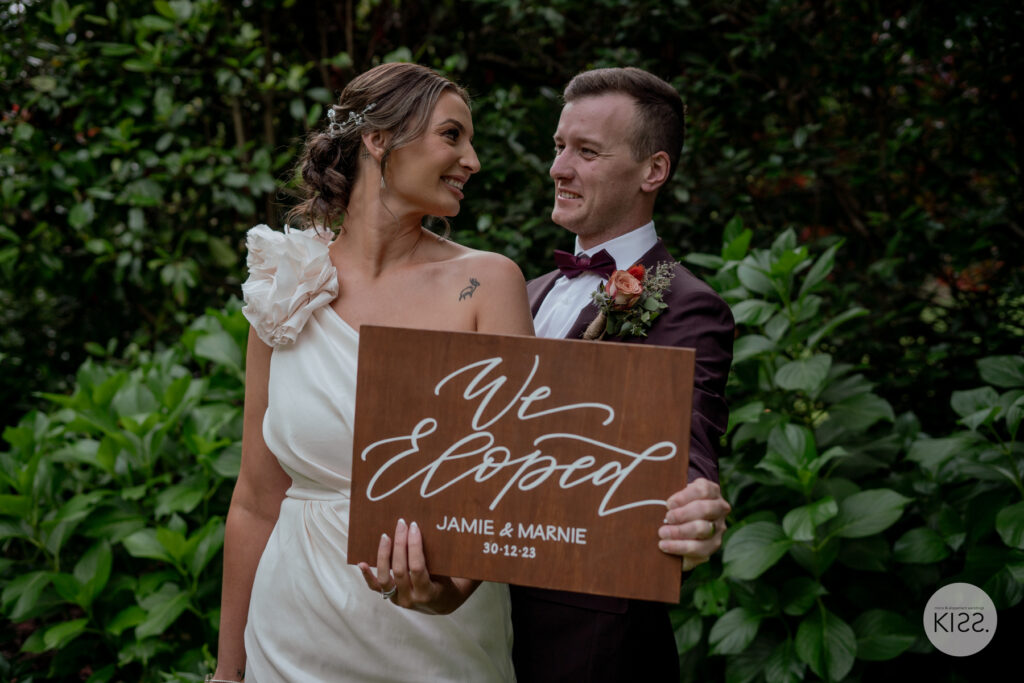 A newly married couple holding a We Eloped sign