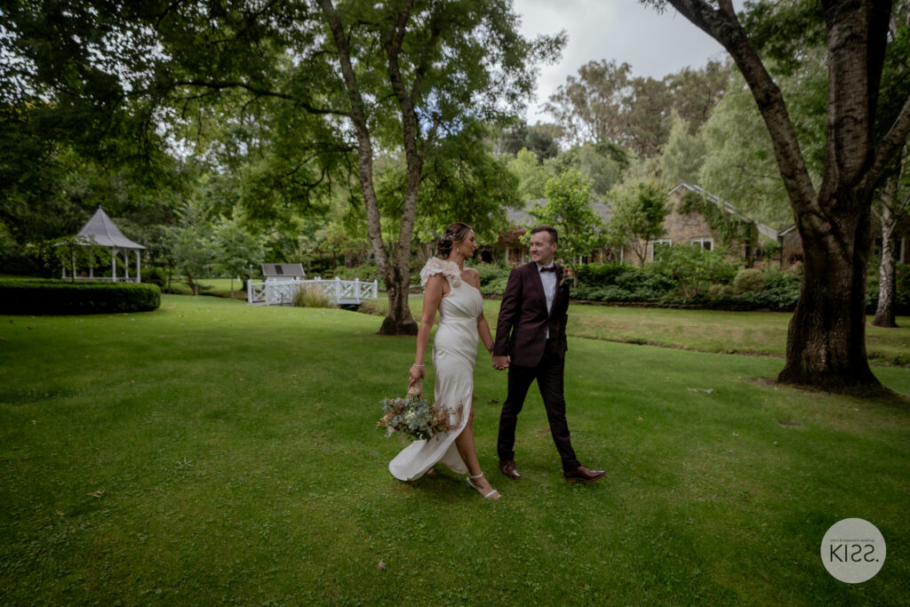 A wedding couple walking across a garden lawn