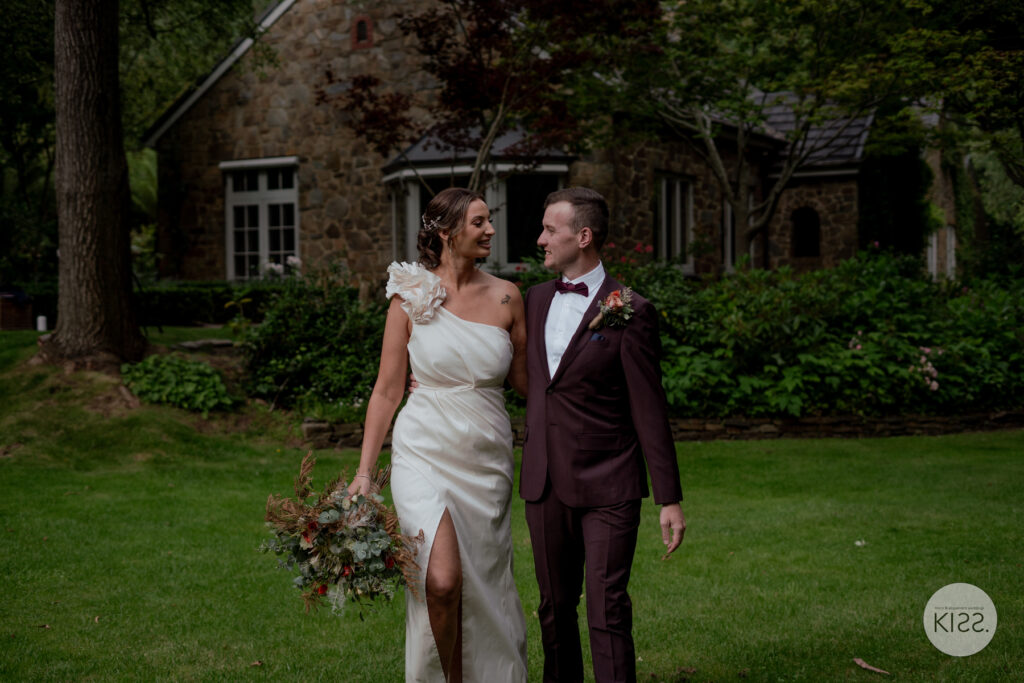 A wedding couple walking beside a stone cottage