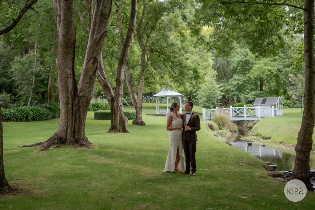 A wedding couple standing together beneath garden trees
