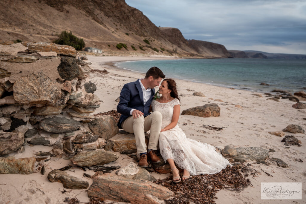 A wedding couple sitting beside a rocky beach