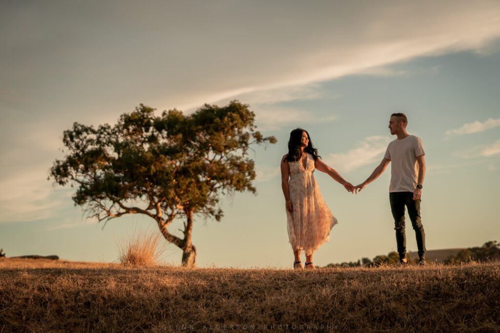 A couple holding hands beside a lone tree at sunset