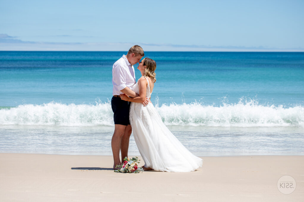 A wedding couple embracing beside turquoise coastal water