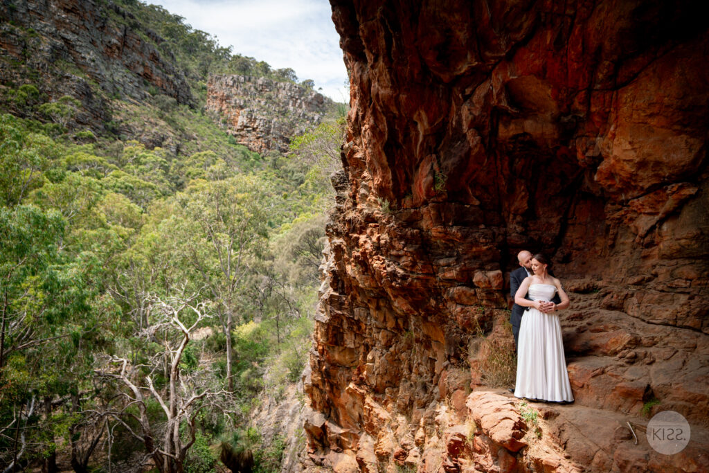 A bride standing beside the orange rock wall of a cave