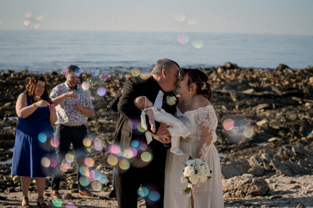 A wedding couple surrounded by bubbles beside the coast