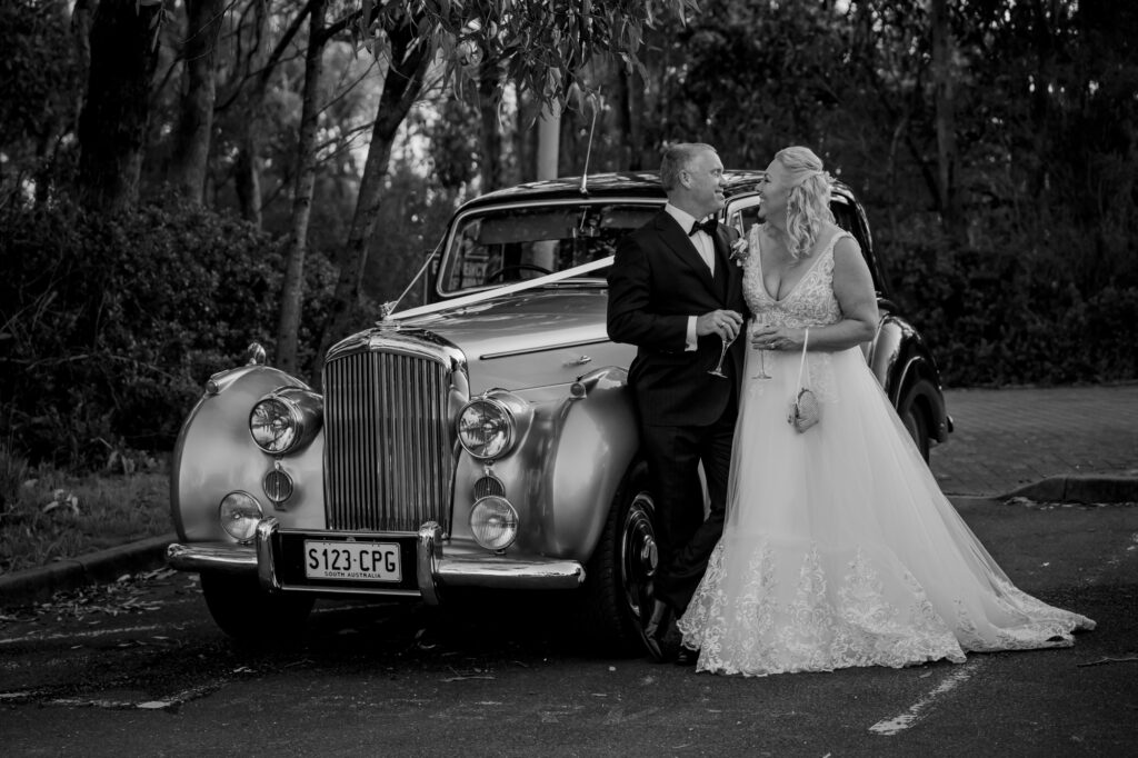 A wedding couple beside a vintage car in black and white