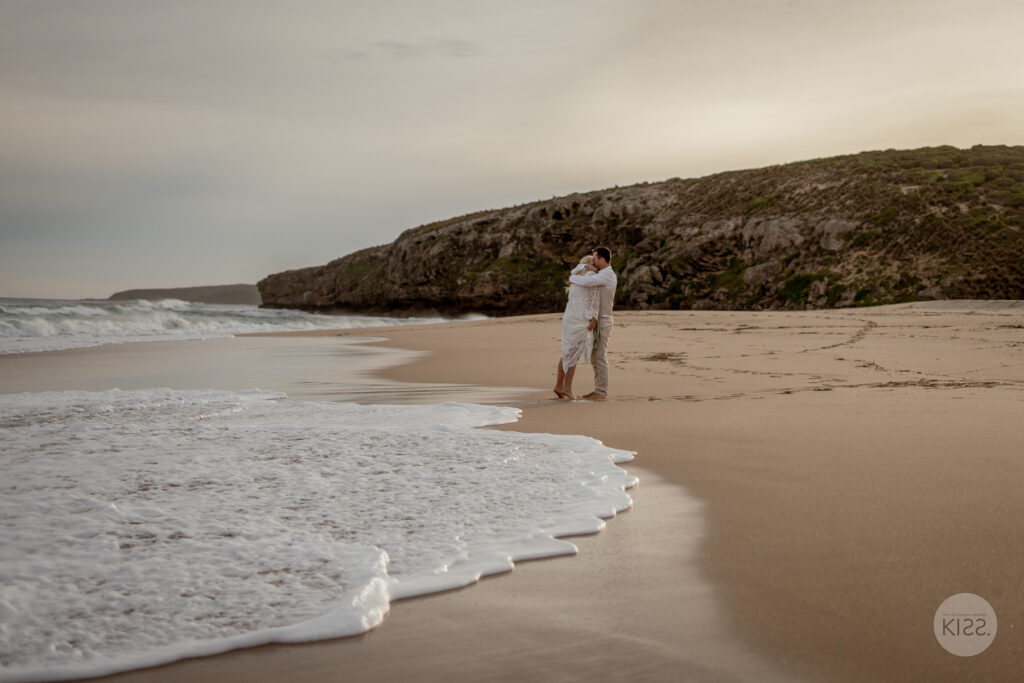 A wedding couple standing together beside the surf