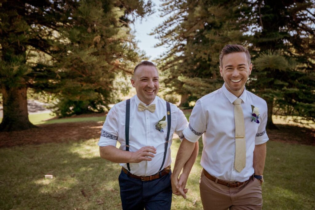 Two grooms smiling together in a garden
