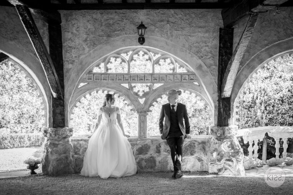 A wedding couple beneath an ornate stone arch in black and white