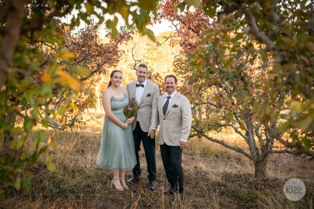 Three people standing together beneath autumn trees