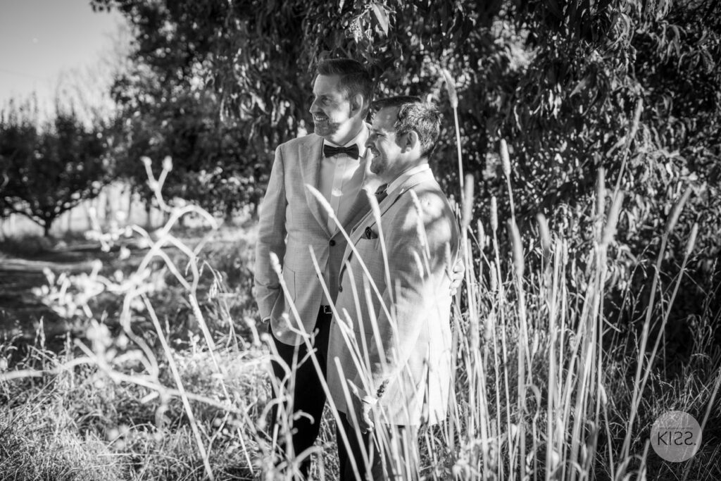 Two grooms among tall grasses in black and white