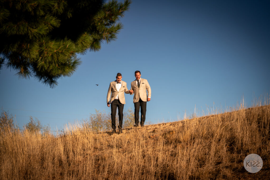 Two grooms walking down a grassy hillside