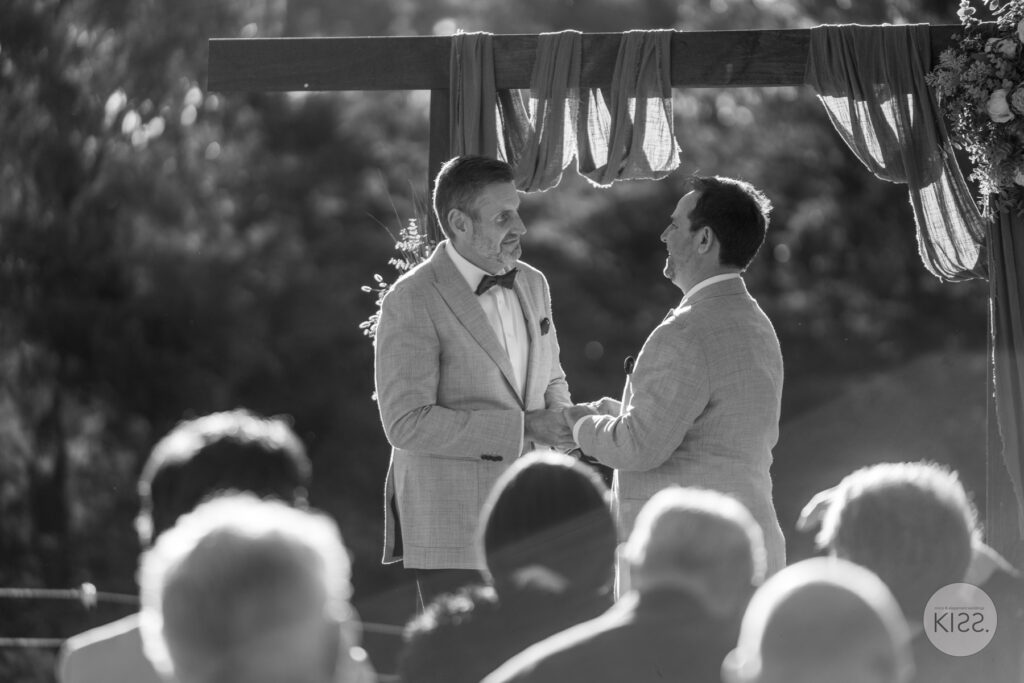 Two grooms exchanging vows in front of their guests in black and white