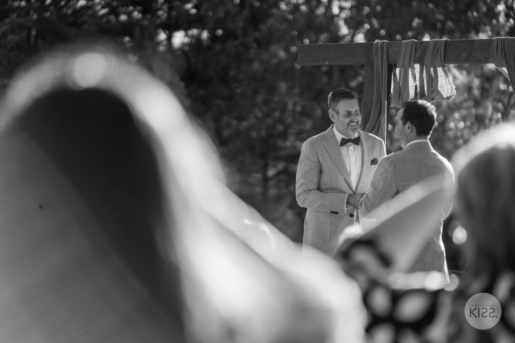 A groom seen past wedding guests during the ceremony in black and white
