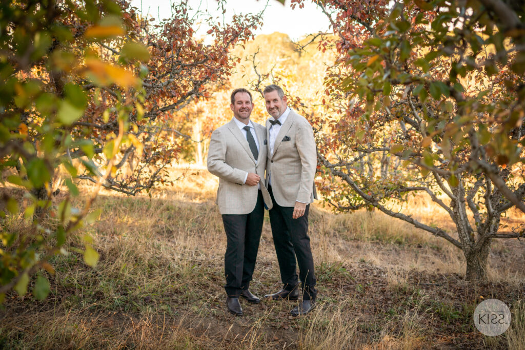 Two grooms standing together among autumn trees