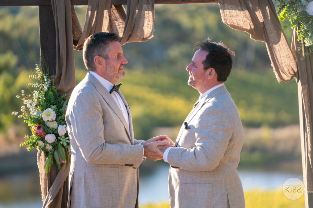 Two grooms smiling and holding hands during their ceremony