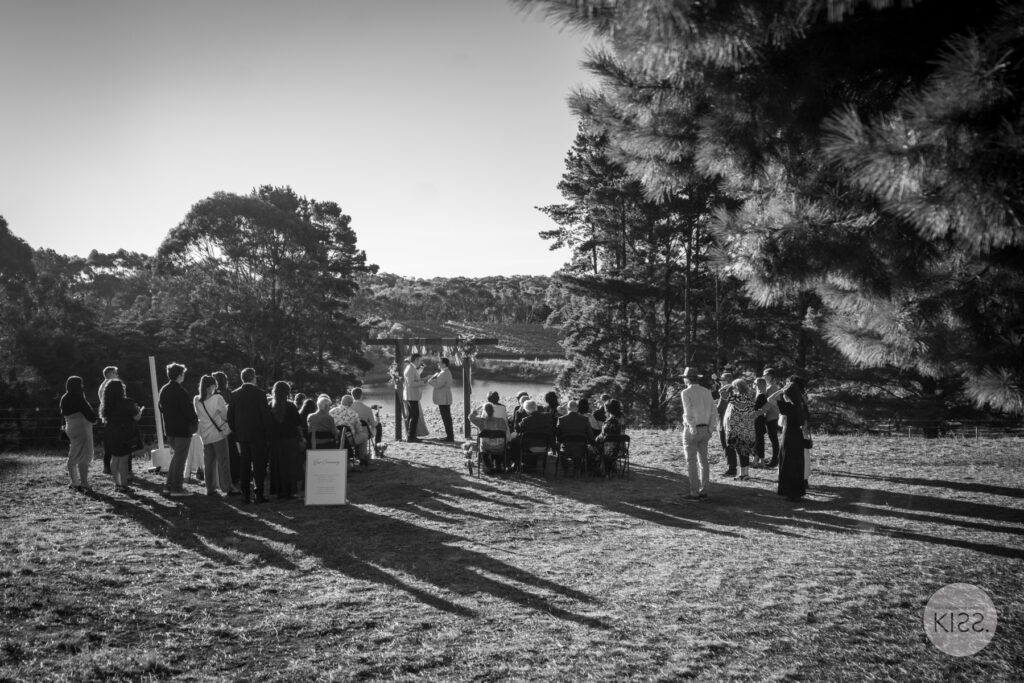 Outdoor wedding ceremony viewed across a lawn in black and white