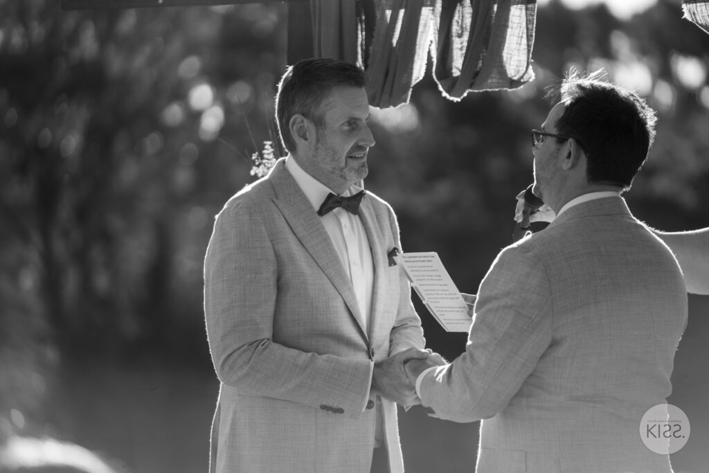 Two grooms holding hands during their vows in black and white