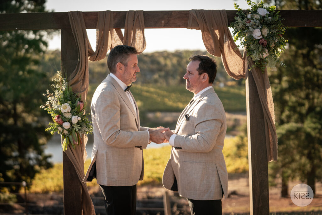 Two grooms exchanging vows beneath a draped arbour