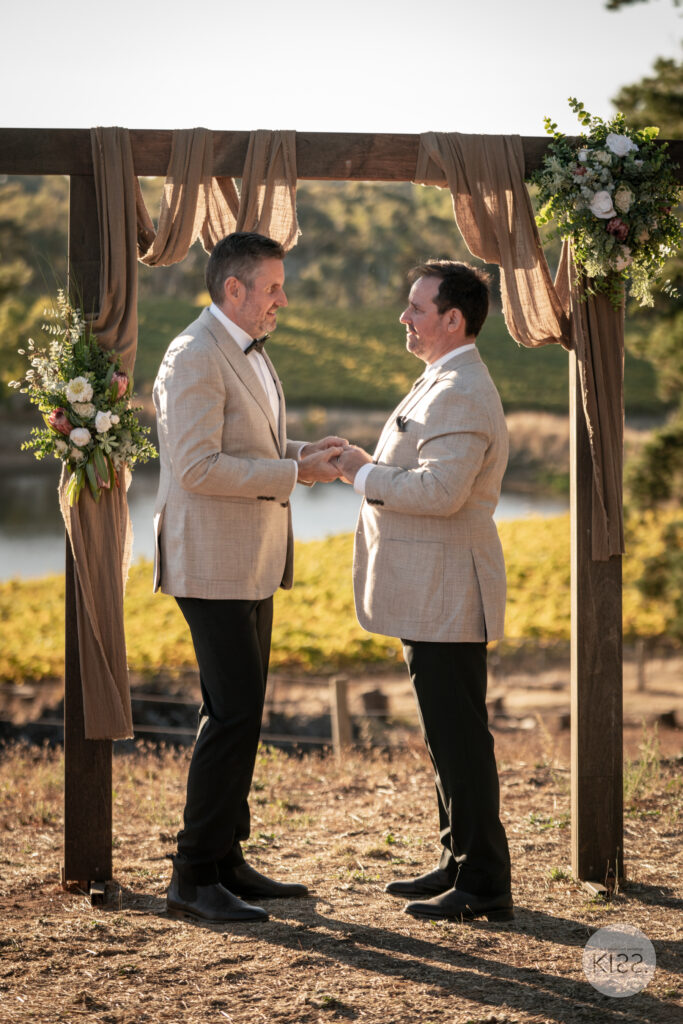 Two grooms exchanging vows beneath a draped arbour