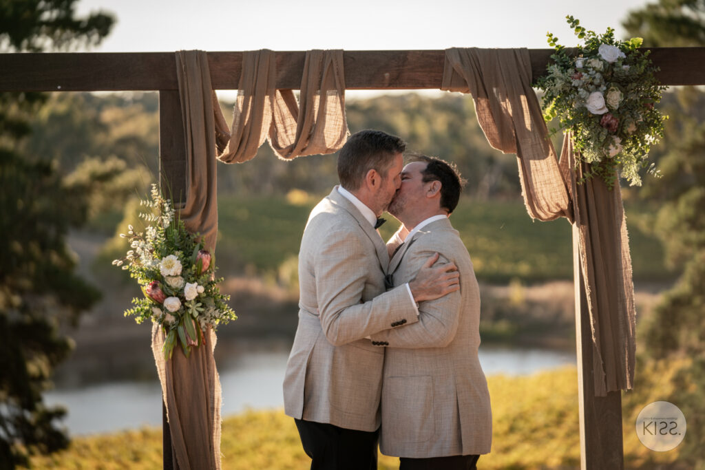Two grooms kissing beneath a wedding arbour