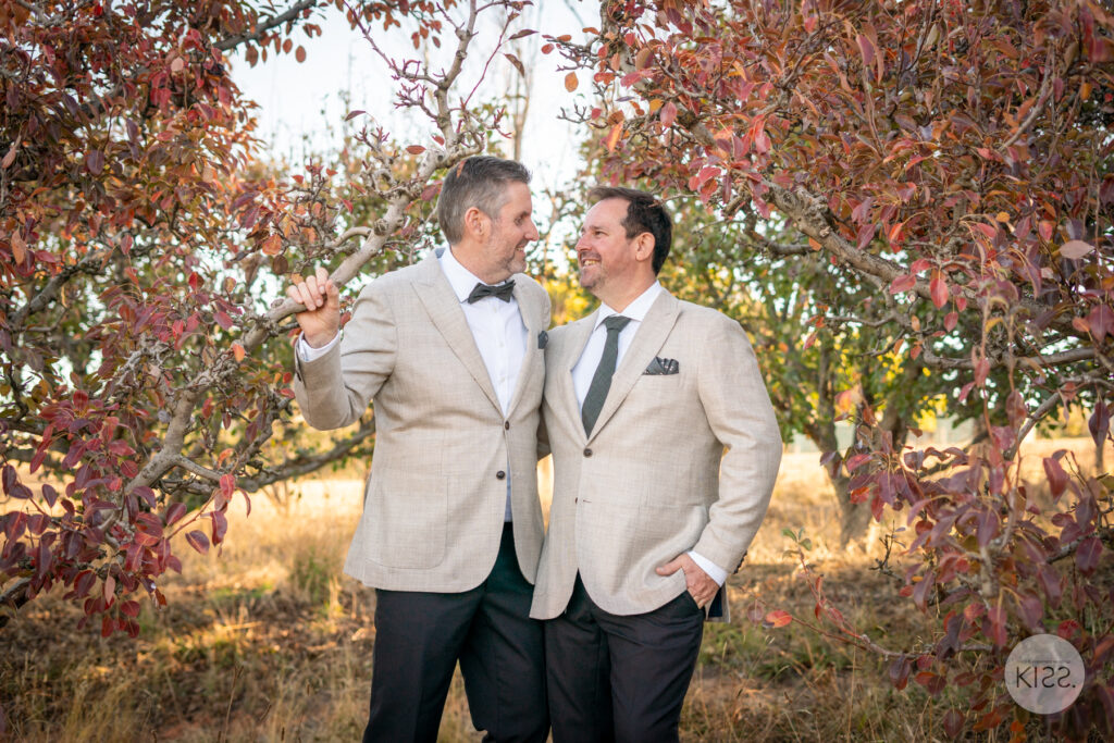 Two grooms standing beneath autumn leaves