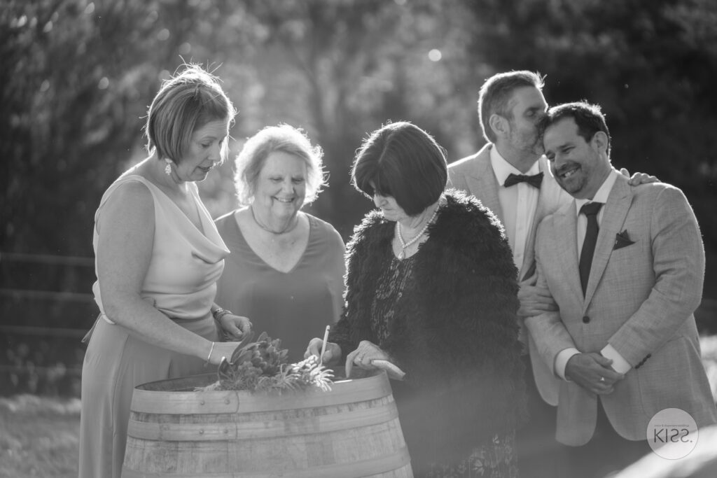 Wedding guests gathered around a bird on a barrel in black and white