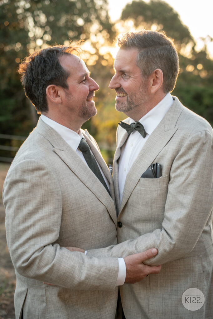 Two grooms smiling at each other outdoors