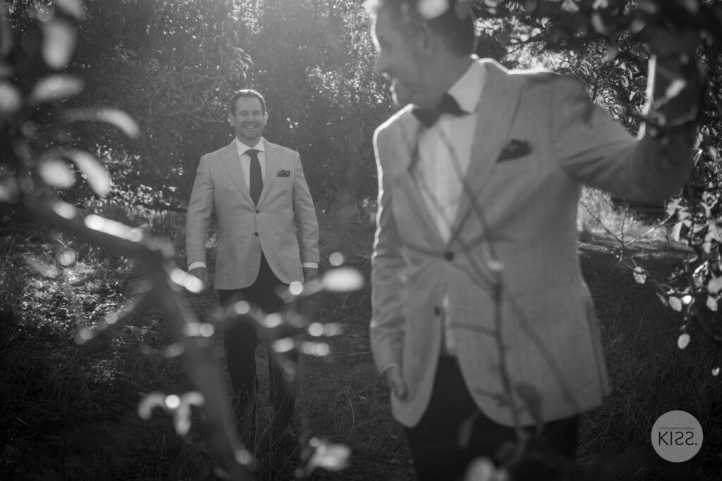 Two grooms walking beneath trees in black and white
