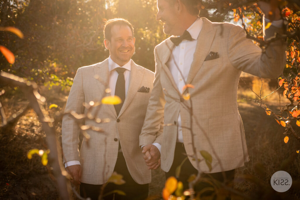Two grooms walking together through sunlit trees